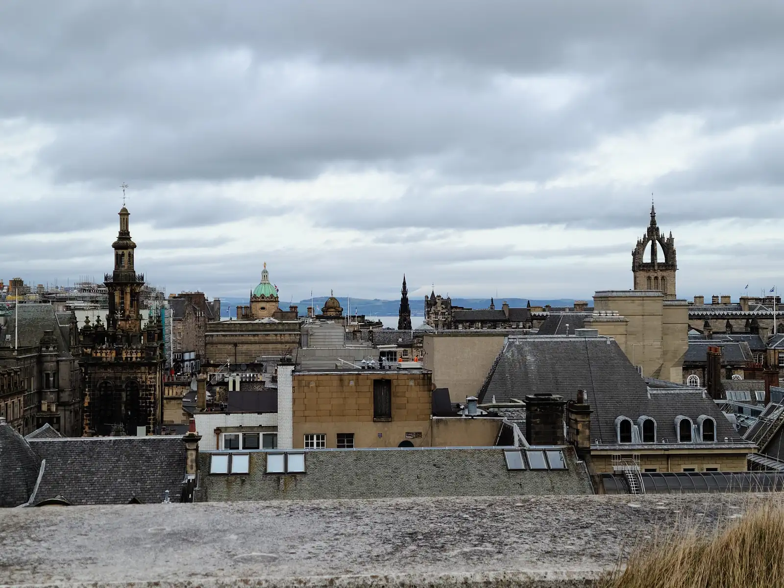 View from Calton Hill across Edinburgh Old Town rooftops with the Tron Kirk steeple and St Giles' Cathedral crown spire under gray skies