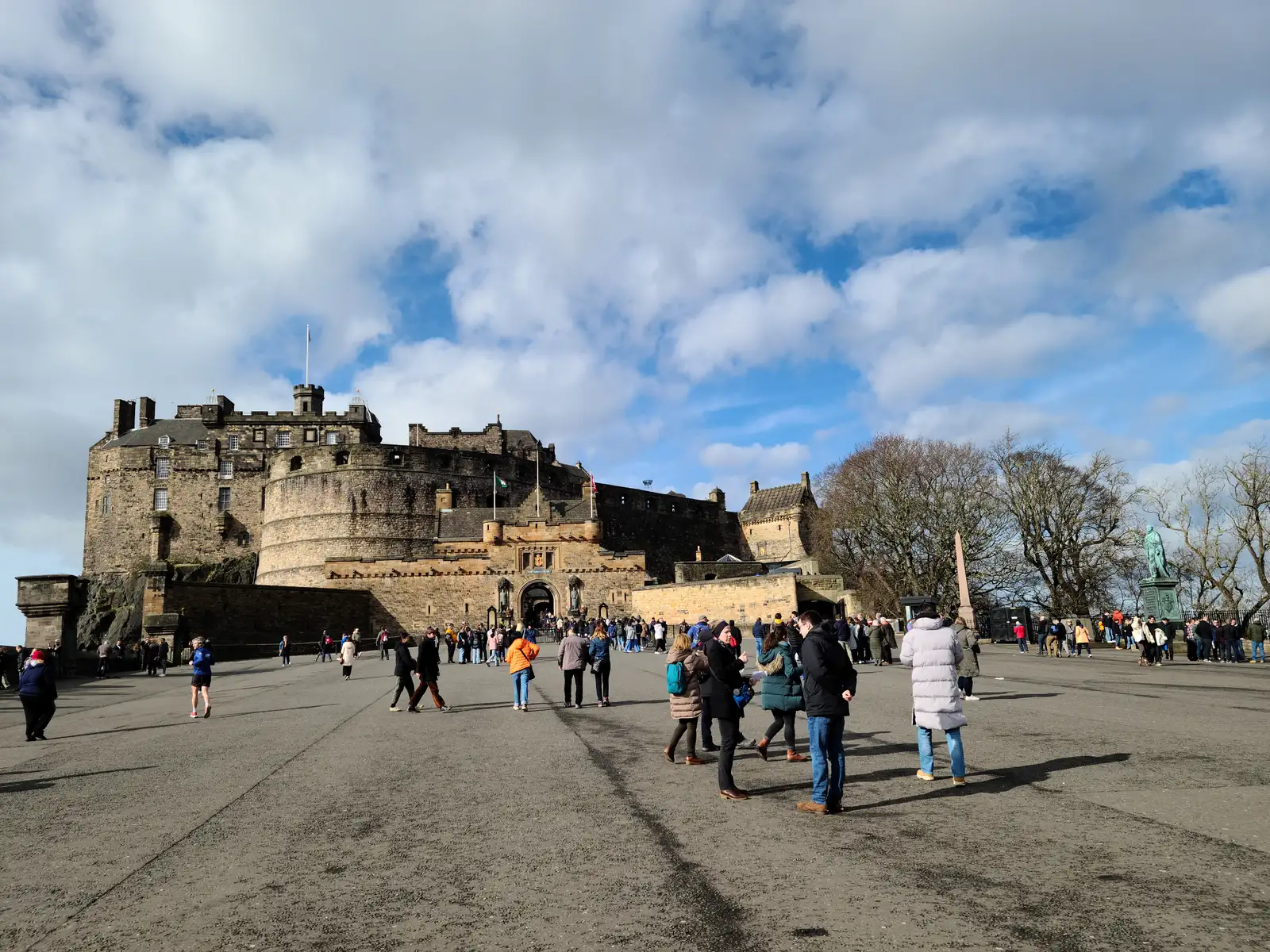 Visitors casting long shadows across Edinburgh Castle Esplanade with the gatehouse and Half Moon Battery under blue winter sky