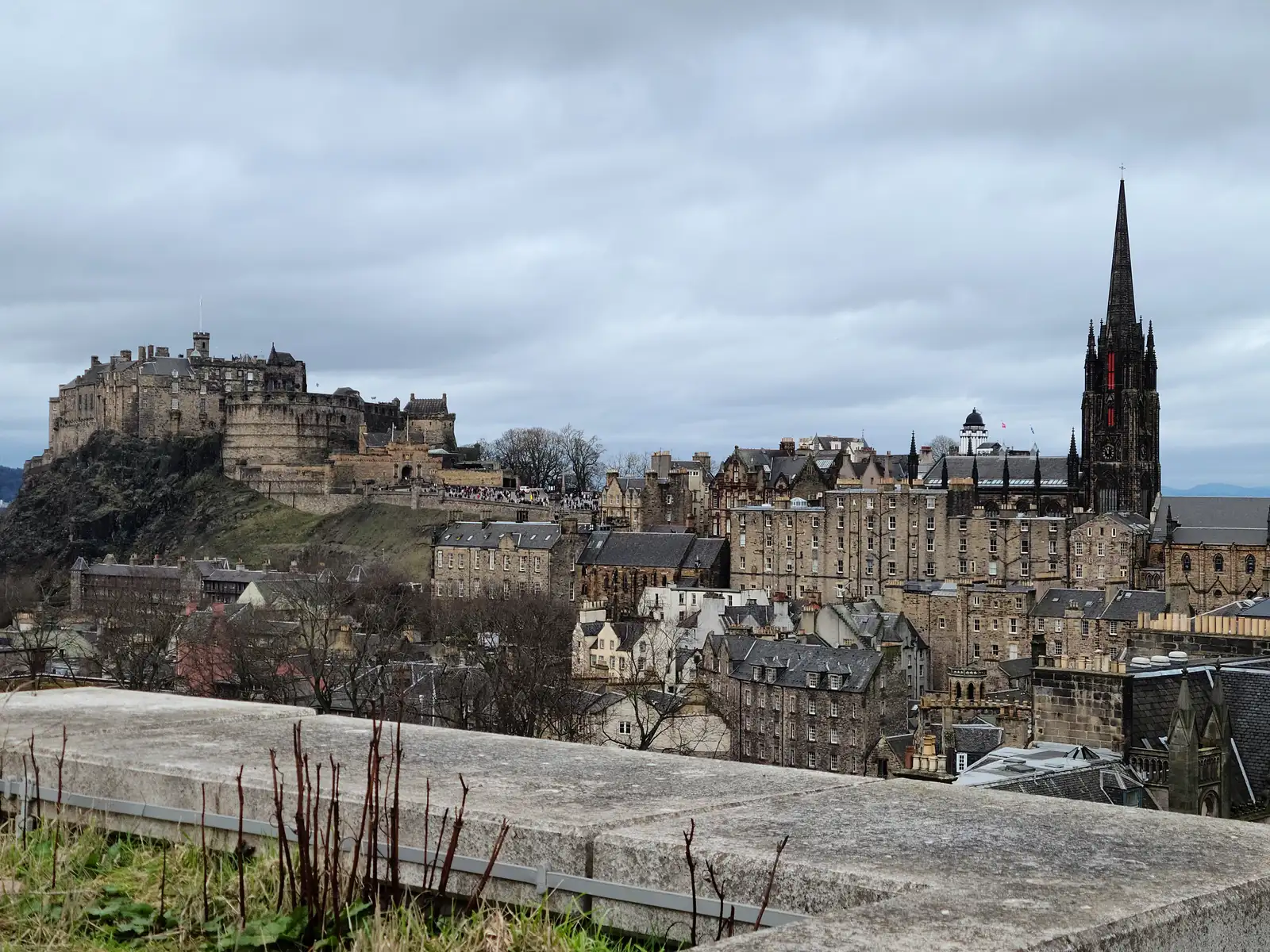 View from Calton Hill of Edinburgh Castle on its crag and the Hub's gothic spire rising above Old Town rooftops under gray skies