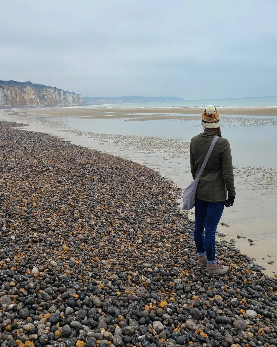 Ashley walking on the pebble beach at Dieppe with white chalk cliffs of Normandy in the distance