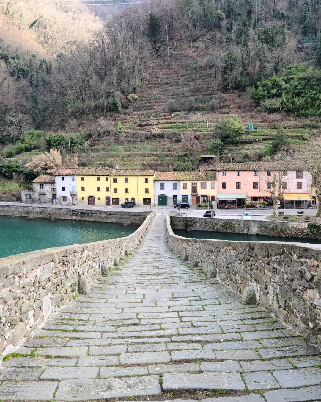 Looking down the stone steps of Devil's Bridge near Lucca, with colorful Italian houses and the green river below